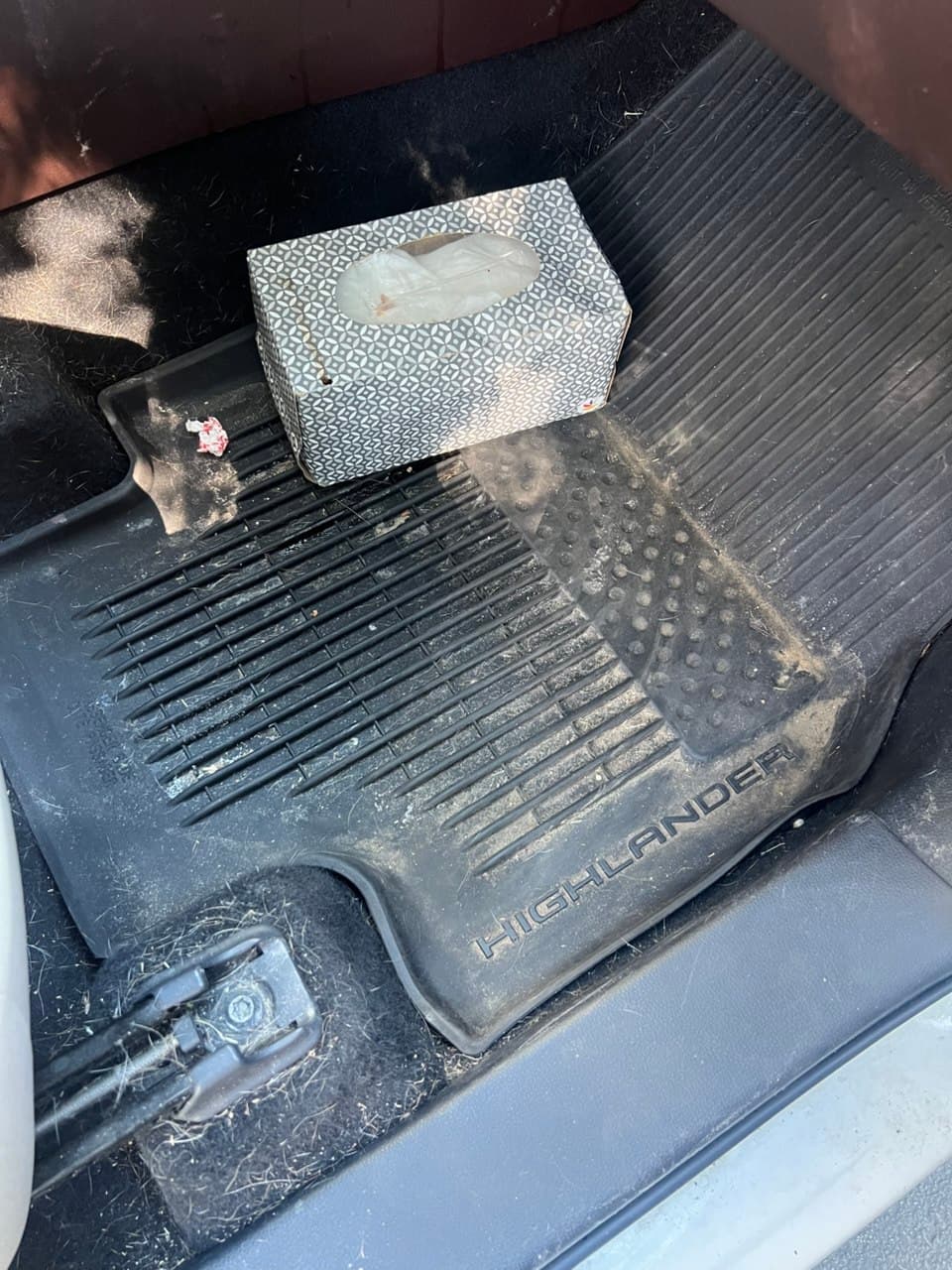 Vehicle footwell with a grimy, debris-covered floor mat before detailing